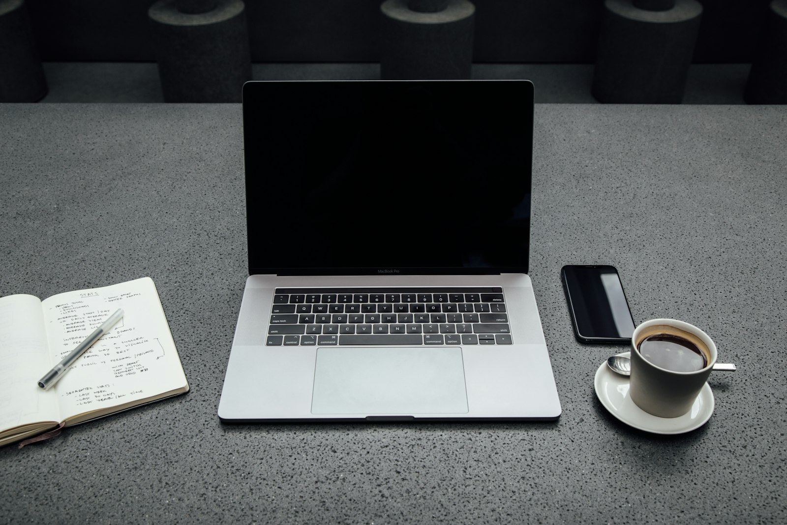 Portátil com café, telemóvel e caderno numa secretária de escritório